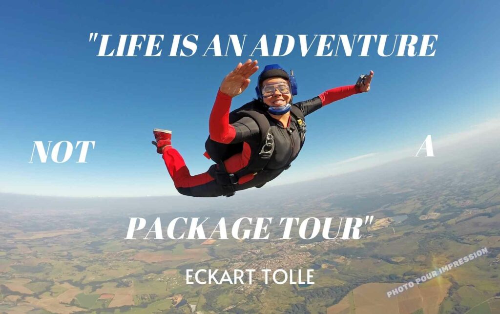 Image représentant une personne en chut libre dans le ciel avec un gros sourire et un parachute dans le dos et avec écrit autour la citation : Life is an Aventure, Not a Package Tour, Eckart Tolle
